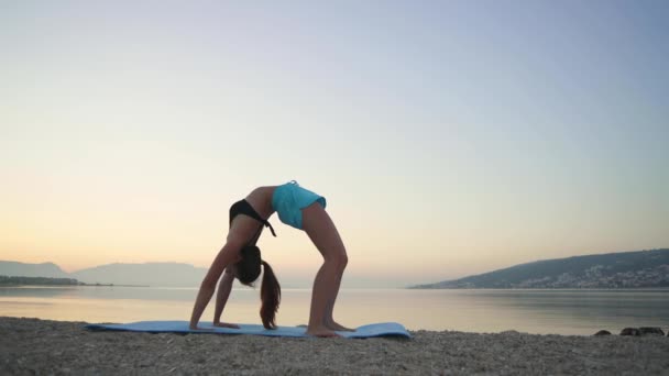 Piękna dziewczyna rozgrzewa się i ćwiczy jogę nad morzem. Jaki sport lubisz najbardziej?, yoga, beach. — Wideo stockowe