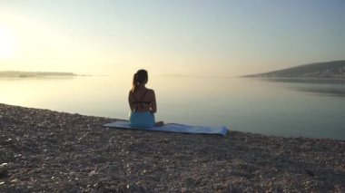 Güzel kız ısınıyor ve deniz kenarında yoga yapıyor. Spor, yoga, plaj, ağır çekim.