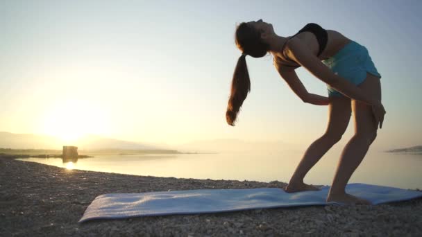 Mooi meisje warmt op en beoefent yoga aan zee. Sport, yoga, strand, slow motion. — Stockvideo