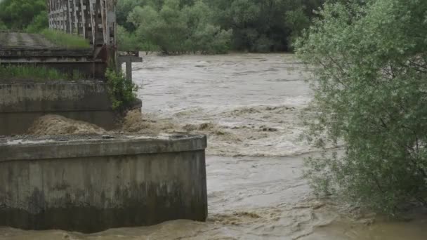 Een oude verlaten brug over een rivier die overstroomt. Stormachtig water stroomt. Extreem hoog waterpeil in de rivier. Natuurramp in het westen van Oekraïne. Langzame beweging — Stockvideo