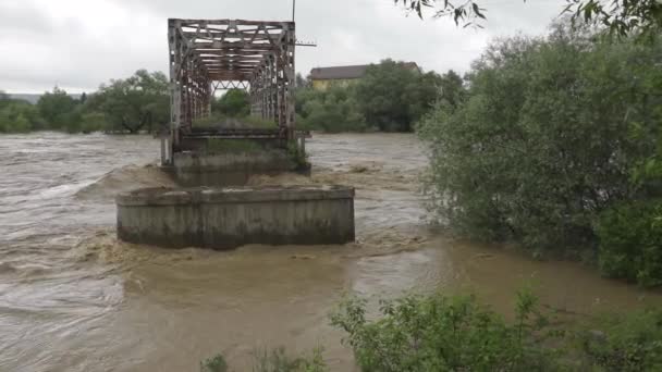 Eine alte, verlassene Brücke über einen Fluss, der über die Ufer tritt. Stürmisches Wasser fließt. Extrem hoher Wasserstand im Fluss. Naturkatastrophe in der Westukraine. — Stockvideo