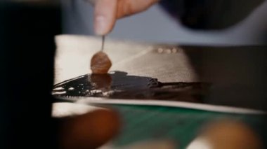 Usta cildine yumuşatıcı krem sürüyor. Gerçek deriden yapılmış bir seyahat çantası üretme süreci. El yapımı. Makro çekim.