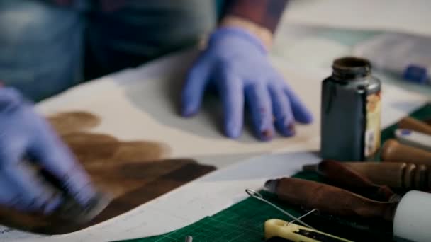 El yapımı deri cüzdan üretme işlemi. Usta bir parça deriyi kahverengiye boyuyor. El yapımı.. — Stok video