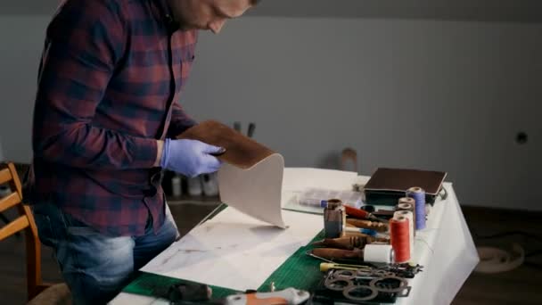 Der Prozess der Herstellung einer handgefertigten Ledertasche. Der Meister untersucht ein Stück bemaltes Leder. Handgefertigt. — Stockvideo