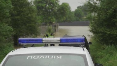 Sel baskınında su basmış bir caddenin arka planında polis arabası parlıyor. Parlayan fenerler yanıp sönüyor. Yağmur yağar ve su seviyesi yükselir..