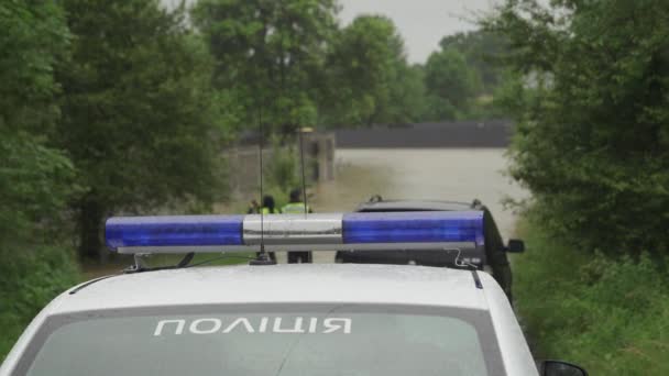 Flitsende politieauto op de achtergrond van een overstroomde straat tijdens een overstroming. Knipperende bakens knipperen. Het regent en het waterpeil stijgt. — Stockvideo