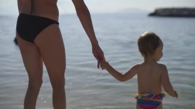 Anne ve küçük kızı suya giriyor. Kadın bebeği eliyle tutuyor. Günaydın Hırvatistan.