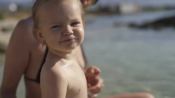 Портрет дворічної дівчинки. Дитина стоїть у воді і посміхається в камеру. Ранкова Хорватія. — стокове відео