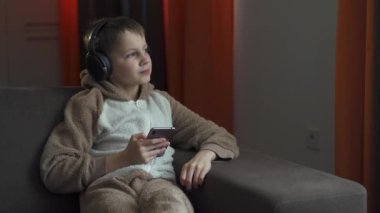 Kulaklıklı ve elinde akıllı telefonla kanepede oturup müzik dinleyen adam. Karantina 2020