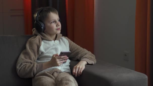 The guy in the headphones and with the smartphone in his hands sits on the couch listening to music. Quarantine 2020 — Stock Video