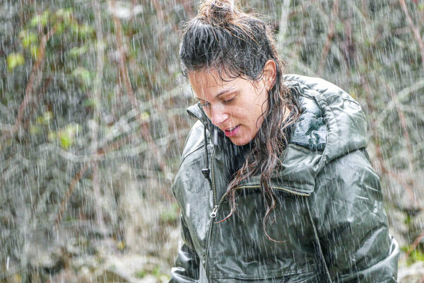 Young latina woman strolling in heavy rain with soaked green jacket and dripping hair