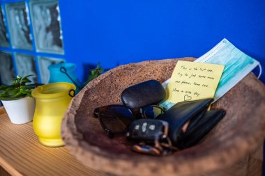 Evin girişindeki küçük masada içinde anahtarlar, cüzdan, maske, güneş gözlüğü ve bir de not olan ahşap bir kutu var.