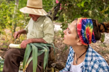 Hasır şapkalı yaşlı adam kütüğün üzerinde sebze keserken torunu ona yardım ediyor.