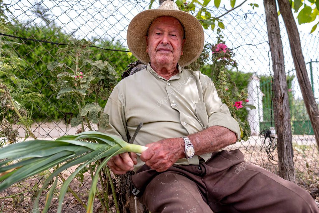 Old man with straw hat cutting vegetables sitting on a log