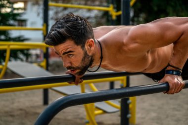 Bir spor salonunun barında, gömleksiz, siyah pantolonsuz ve maske takan genç bir Latin adamın yakın portresi.