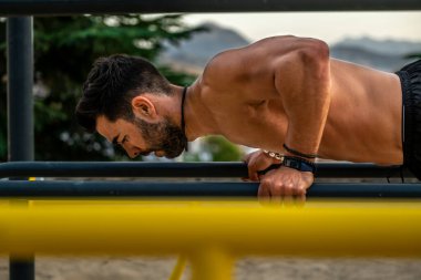 Bir spor salonunun barında, gömleksiz, siyah pantolonsuz ve maske takan genç bir Latin adamın yakın portresi.