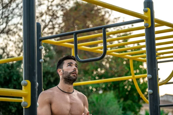 Bir spor salonunun barında, gömleksiz, siyah pantolonsuz ve maske takan genç bir Latin adamın yakın portresi.