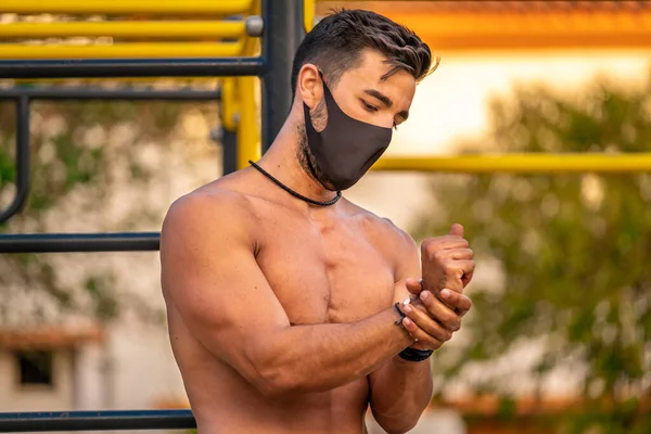 Gömleği ve siyah pantolonu olmayan ve ellerini hidroseksüel jel ile dezenfekte eden genç Latin bir adam.