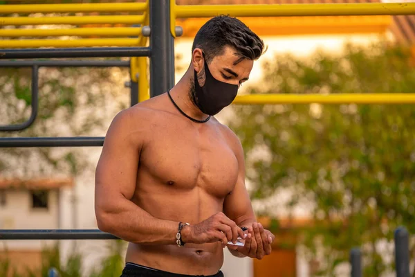 Gömleği ve siyah pantolonu olmayan ve ellerini hidroseksüel jel ile dezenfekte eden genç Latin bir adam.