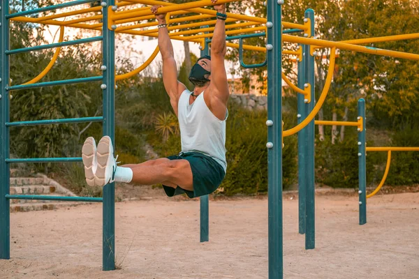 Soluk mavi tişörtlü, siyah pantolonlu ve maskeli genç bir Latin jimnastik parkında egzersiz yapıyor.