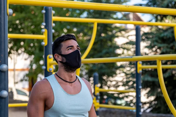 Soluk mavi tişörtlü, siyah pantolonlu ve maskeli genç bir Latin jimnastik parkında egzersiz yapıyor.