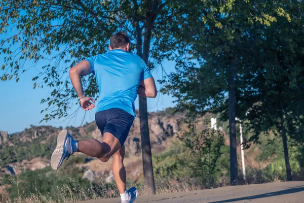 Mavi tişörtlü genç bir adam ve mor gömlekli genç bir kadın parkta arka planda ağaçlarla koşuyorlar.
