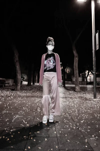 Woman walking alone through the park at night with a face mask during the coronavirus pandemic