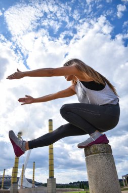 Sporcu kadın tek bacağıyla dışarıda çömeliyor.