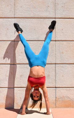 Duvara yaslanan kız başını eğip omuzlarını eğiyor.