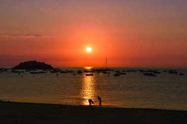 Costa Brava 'da güneş doğarken sahilde eğlenen iki arkadaşın silueti..