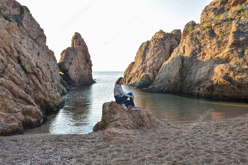 Woman on vacation sitting on a rock in front of the sea.