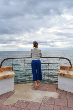 Fırtınalı bir günde çıplak ayakla arkadan fotoğraflanmış bir kadın denize bakıyor..