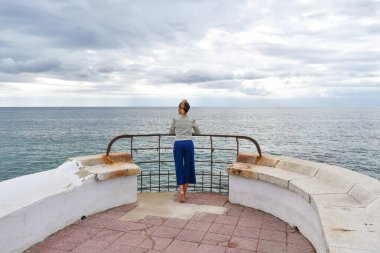 Fırtınalı bir günde çıplak ayakla arkadan fotoğraflanmış bir kadın denize bakıyor..