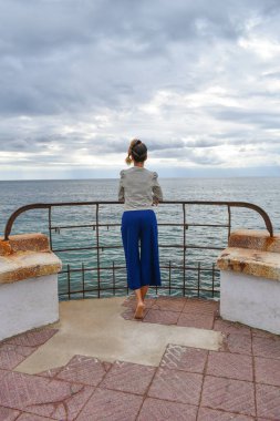 Fırtınalı bir günde çıplak ayakla arkadan fotoğraflanmış bir kadın denize bakıyor..