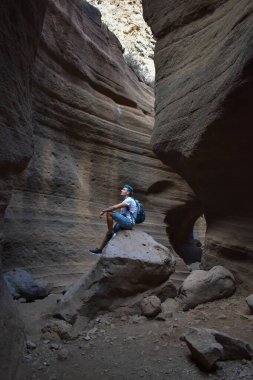 Genç adam bazı pürüzsüz ve renkli volkanik taşların üzerinde oturuyor, Tobas de Colores, Barranco de las Vacas.