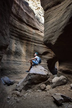 Genç adam bazı pürüzsüz ve renkli volkanik taşların üzerinde oturuyor, Tobas de Colores, Barranco de las Vacas.