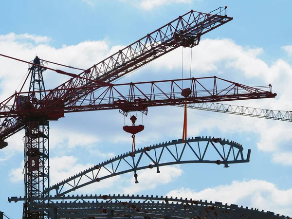 Construction cranes lift construction farms of complex construction against the sky and cloud