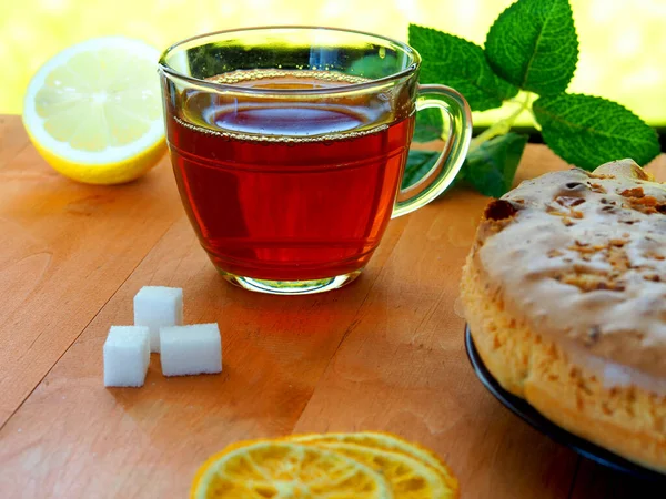 Hot tea in a glass mug in the summer on a wooden table with lemon, cake and sugar.