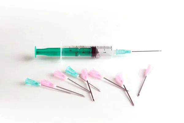 Syringe and different syringe needles on a white surface