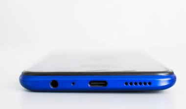 Yakın plan, USB tip C şarj portu, 3.5 mm hoparlör jack, beyaz arkaplanda mavi akıllı telefonun altında mikrofon.