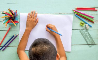 Çocuğun üst görünümü beyaz kağıda renkli kalemler çiziyor..