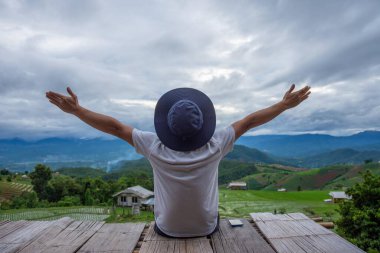 İki kollu şapka takan bir adam mutluluk, başarı ve manzaranın güzelliğini gösterir..