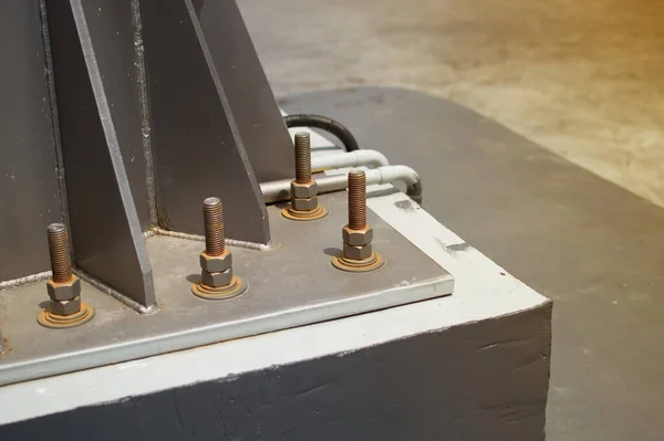 Uzun cıvatalar çelik kolonlara bağlı. Büyük beton bloklar, ışık direkleri var..