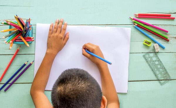 Верхний вид мальчика использует цветные карандаши, чтобы рисовать на белой бумаге..