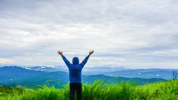 Mutlu bir gezgin, çimlerin üzerinde durmuş, güzel dağ manzarasına hayran kalmış. İnsanlar doğanın tadını çıkarır.