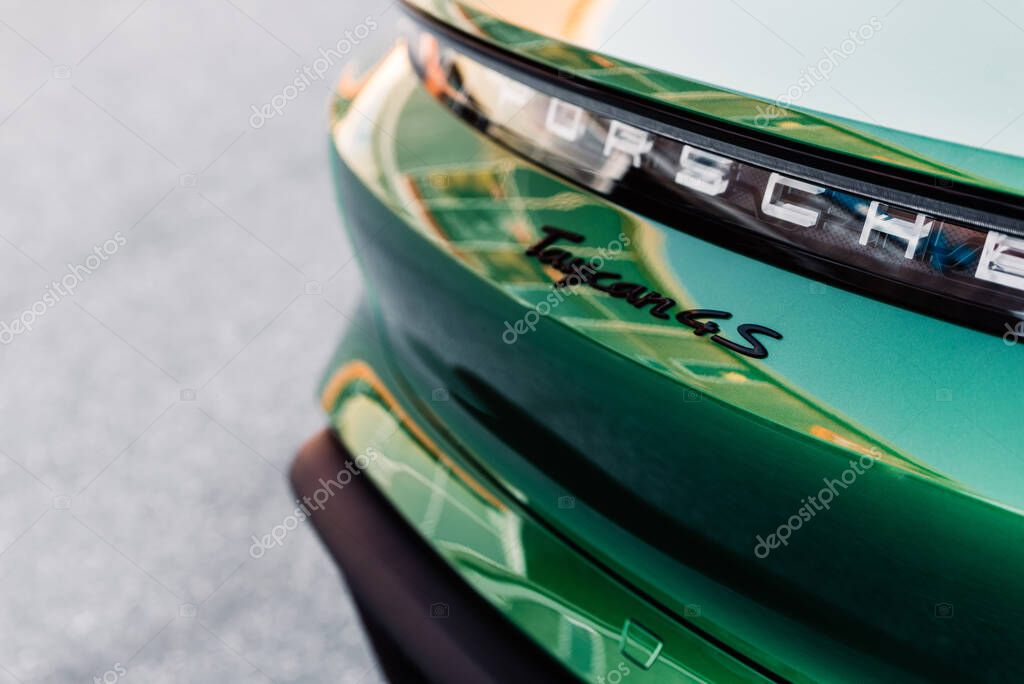 Alesund / Norway - May 31, 2020: Green luxury Porsche Taycan sedan in a parking lot, parked for promotional purposes. Logo detail shot.
