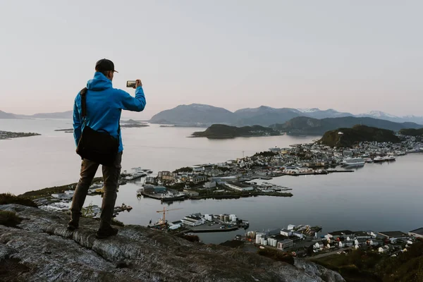 Gezgin dağdan manzaralı Norveç şehir manzarasının fotoğraflarını çekiyor. Seyahat ve yürüyüş konsepti. Mavi saatte çekilmiş.. 