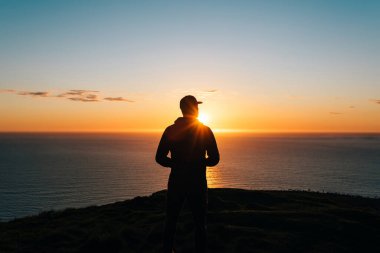 Gün batımında ufka bakan genç adamın silueti. Uçurumdan atılmış.