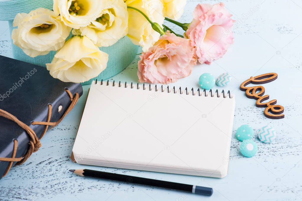 Yellow eustoma flowers and open notebook on blue table. Greeting card for Birthday, Womens or Mothers Day