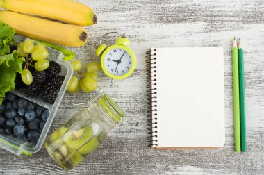 Boş defter ve beslenme çantası ve ahşap masa üzerinde meyve çilek